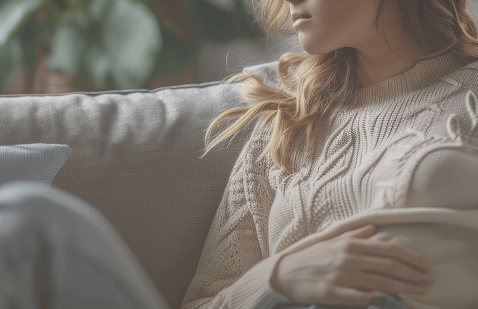 Woman wearing a cozy knitted sweater sitting on a sofa, representing relaxation, home comfort, and a moment of quiet rest