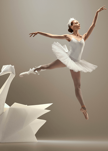 allerina performing a jump next to a large origami swan structure, symbolizing physical lightness and freedom of movement