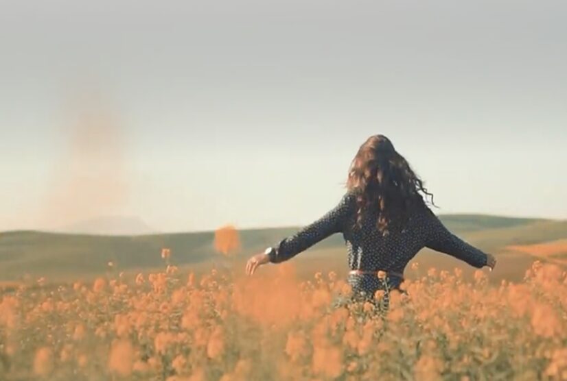 Woman walking through a field of yellow flowers with open arms, symbolizing freedom, well-being, and relief from discomfort